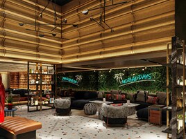 A modern lounge area with a high ceiling, patterned walls, and a neon sign reading 'NOBADAYS'.