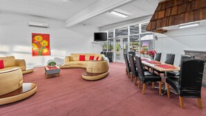 A spacious room with a curved sofa, a dining table with chairs, and a flat-screen TV mounted on the wall. - Torrumbarry Motel (Torrumbarry)