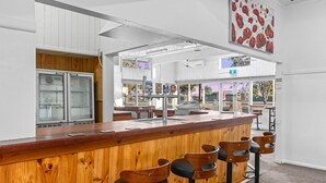 A modern bar area with wooden bar counter and stools, glass display cases, and a large floral artwork on the wall. - Torrumbarry Motel (Torrumbarry)