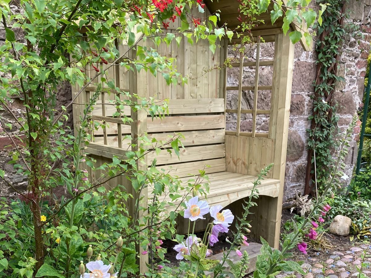 Un banc en bois dans un jardin, avec des murs en pierre et différentes plantes.