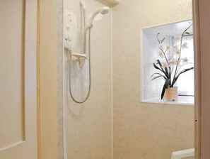 A bathroom with a shower, a window with an orchid plant, and a wall-mounted control panel.