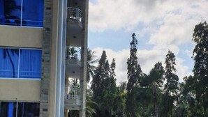 A swimming pool with a curved edge, surrounded by a brick walkway. There is a multi-story building with balconies and a person standing near the pool. - Stay.Plus Bamburi Beachfront Apartment (Mombasa)