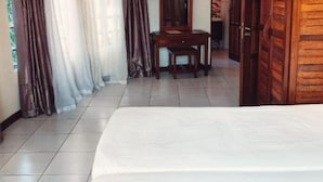 A hotel room with a large bed, a wooden wardrobe, a small table with a mirror, and curtains on the windows. - Stay.Plus Bamburi Beachfront Apartment (Mombasa)
