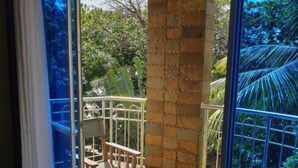 A balcony with a stone pillar, a metal railing, and a view of greenery. - Stay.Plus Bamburi Beachfront Apartment (Mombasa)