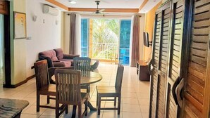 A room with a sofa, chairs, a table, and a balcony with a view of greenery. - Stay.Plus Bamburi Beachfront Apartment (Mombasa)