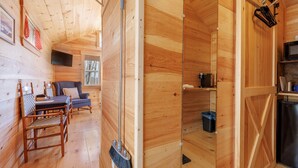 A wooden cabin interior with a dining area, a sofa, a TV mounted on the wall, and a kitchen area with a refrigerator. - Quiet Maine Cabin 2 • Hideaway in the Trees • Sauna (Stockton Springs)