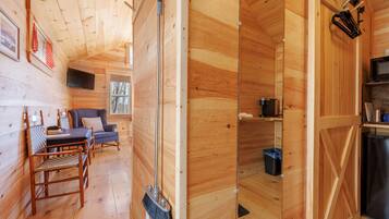 Ein Holzblockhaus-Interieur mit Essbereich, einer Couch, einem an der Wand montierten Fernseher und einer Küchenzeile mit Kühlschrank.