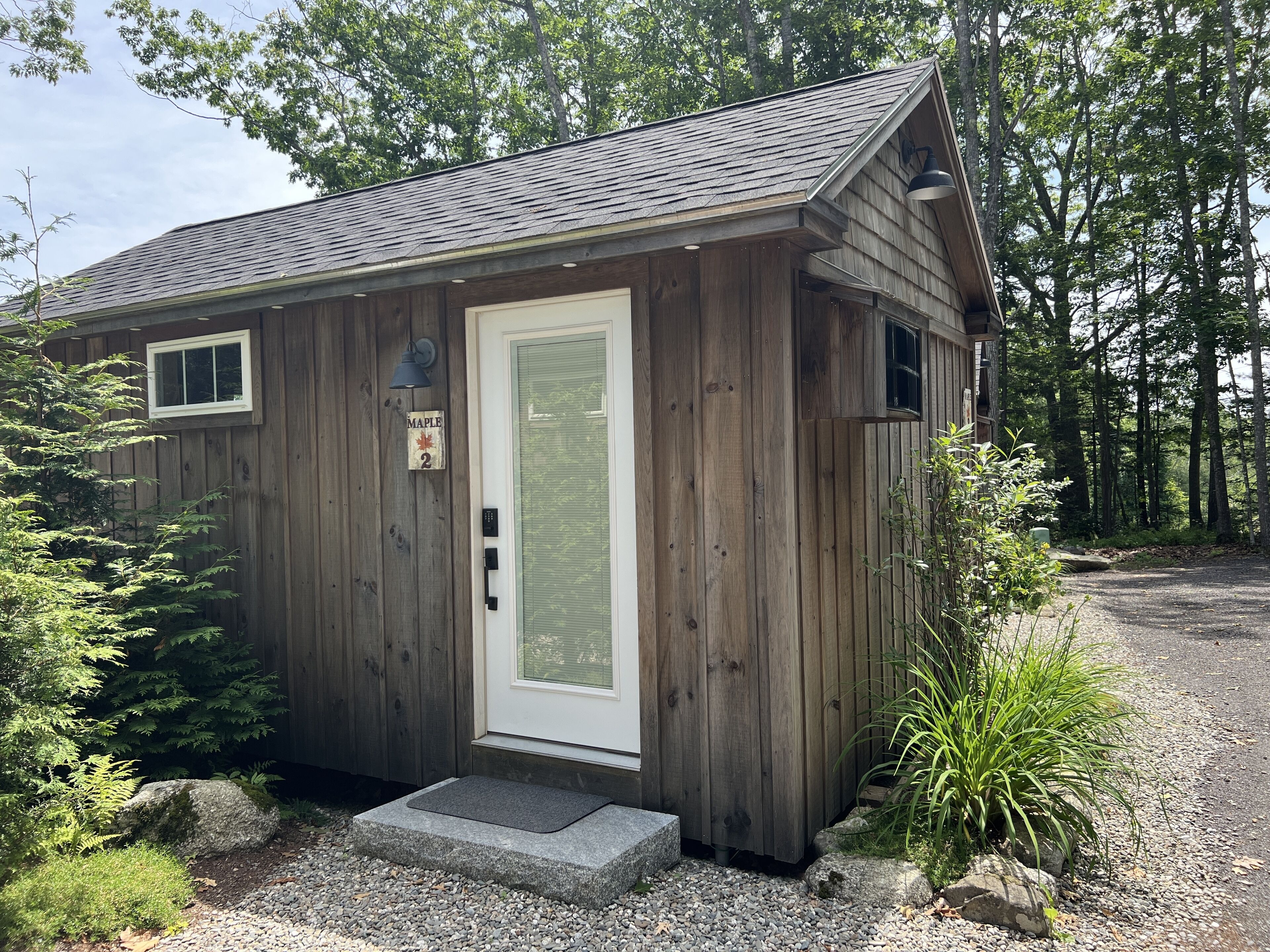 A small wooden cabin with a white door, a mailbox, and a mailbox number sign.