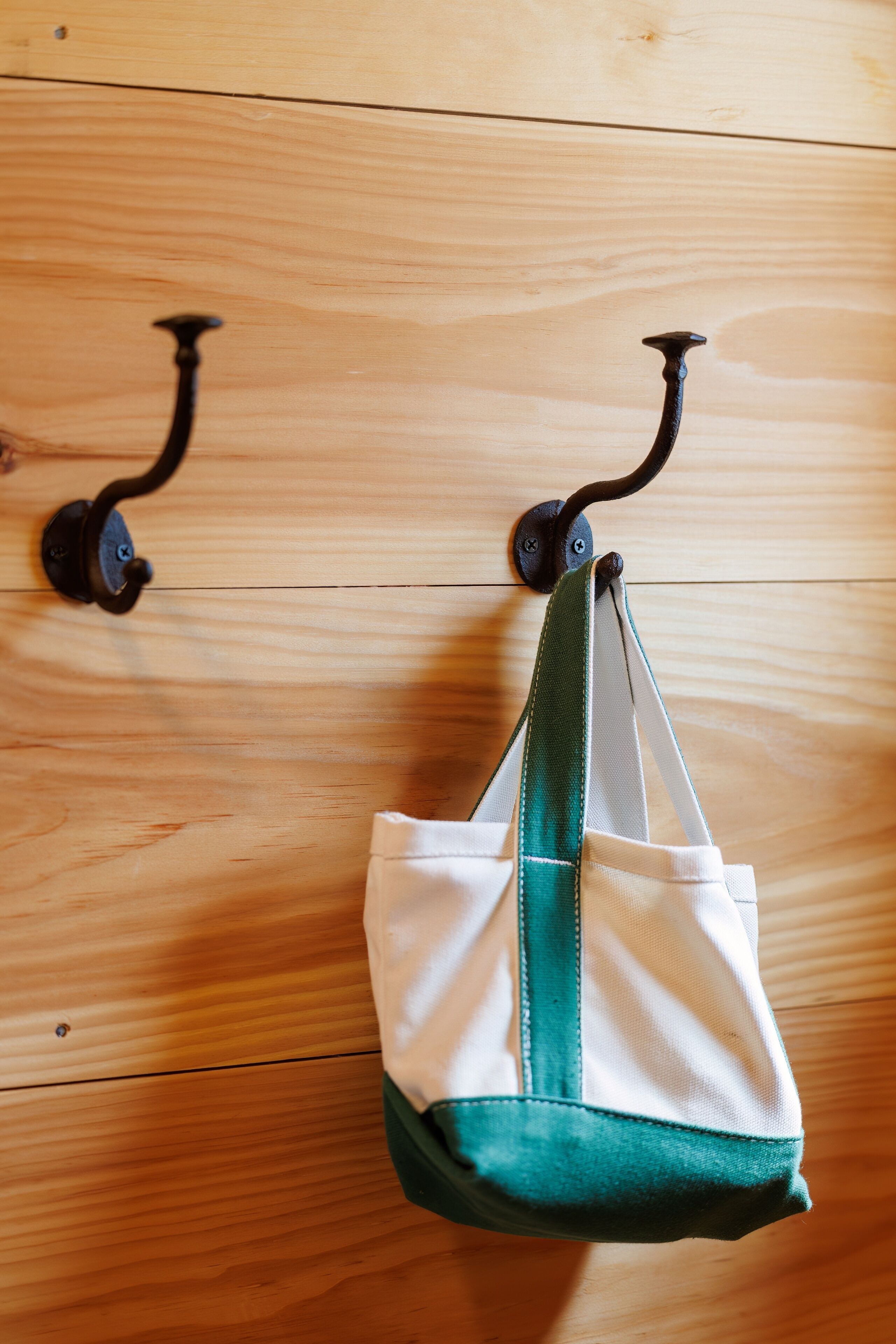 A wooden floor with two metal hooks and a white bag with green accents hanging from one of the hooks.