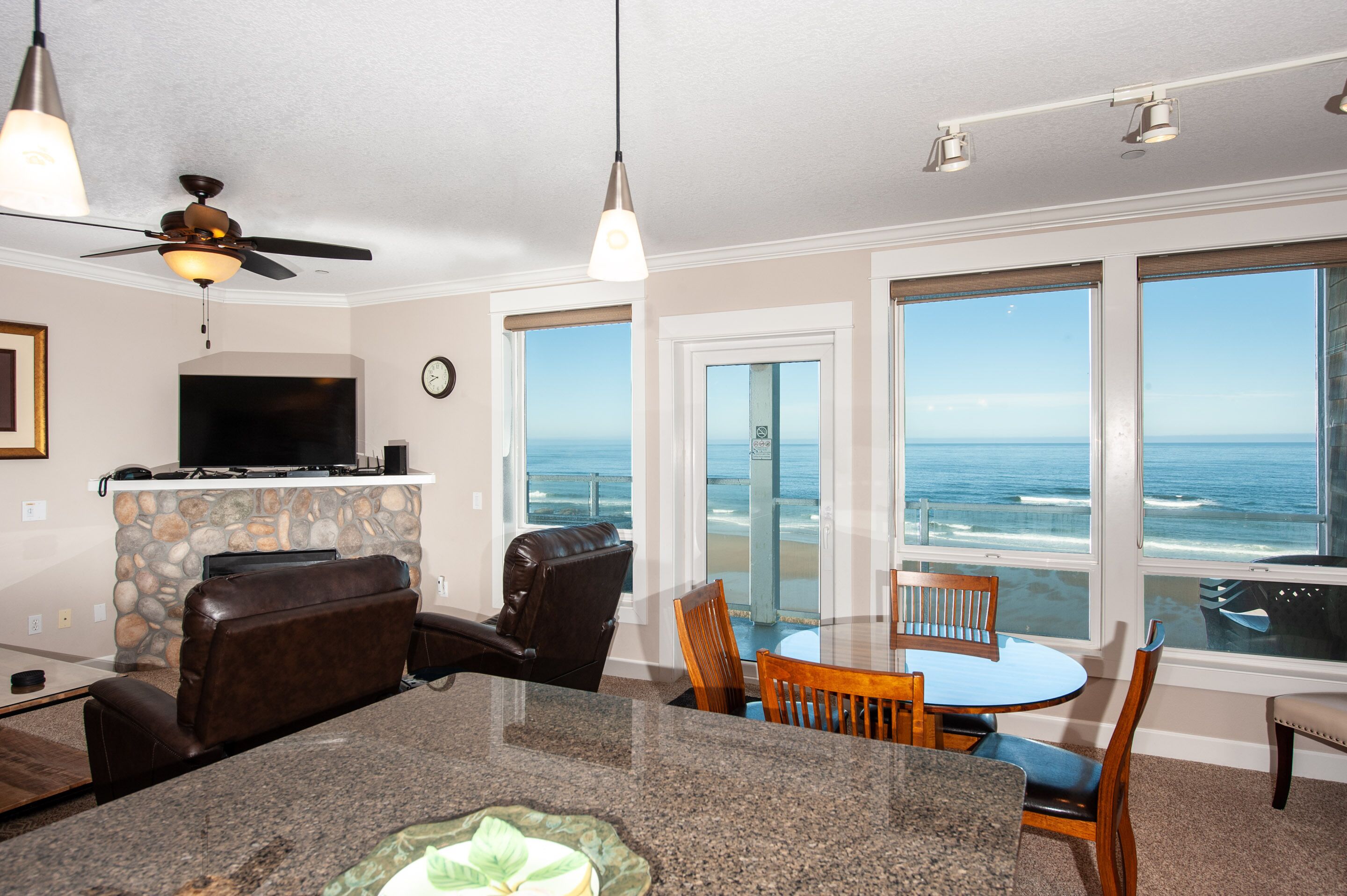 A modern living room with a stone fireplace, a flat-screen TV, and a large window overlooking the ocean.
