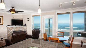 A modern living room with a stone fireplace, a flat-screen TV, and a large window overlooking the ocean.