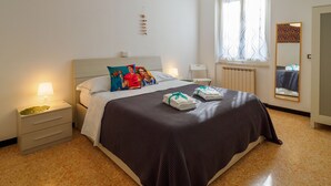 A neatly arranged bedroom with a bed, bedside tables, a hanging light fixture, a window with curtains, and a mirror on the wall. - La Casa di Frida Family Apartment (Vernazza)