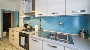 A modern kitchen with white cabinets, a stainless steel sink, and a blue tiled backsplash. - La Casa di Frida Family Apartment (Vernazza)