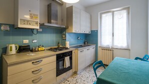 A compact kitchen with a gas stove, a kettle, and a toaster. There is a window with a curtain, a sink, and cabinets. - La Casa di Frida Family Apartment (Vernazza)