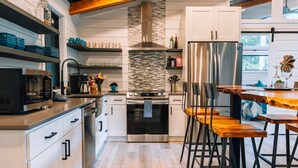 A modern kitchen with white cabinets, a stainless steel refrigerator, a built-in oven, and a wooden dining table with bar stools. - I'll Have S'More - Hocking Hills -Lux In & Out (Hocking Hills)