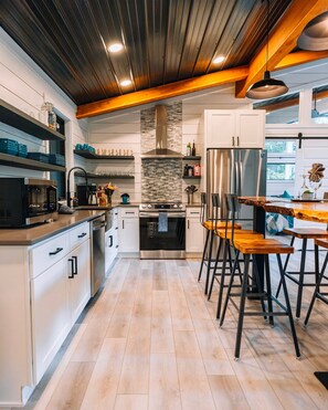 Una cocina moderna con armarios blancos, un refrigerador de acero inoxidable, horno empotrado y una mesa de comedor de madera con taburetes de bar.