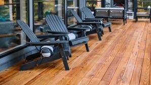 A wooden deck with Adirondack chairs, a stone fireplace, and large windows offering a view of trees. - I'll Have S'More - Hocking Hills -Lux In & Out (Hocking Hills)