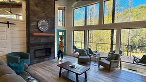 A spacious living room with a fireplace, large windows, and a view of the outdoors. - I'll Have S'More - Hocking Hills -Lux In & Out (Hocking Hills)