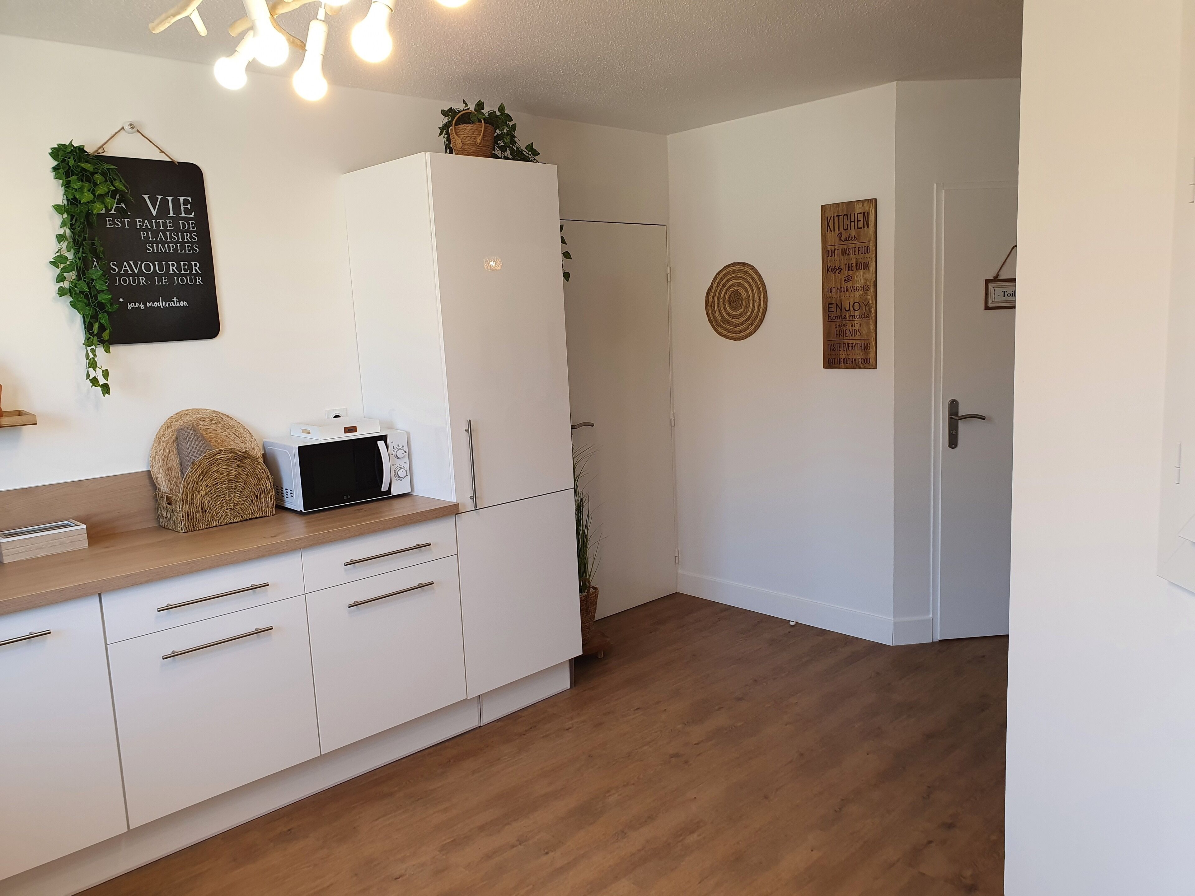 A modern kitchen with white cabinets, a microwave, and a wooden countertop. There are decorative items on the countertop and a sign on the wall.