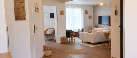 A modern living room with a sofa, a dining table, and a TV. There are wicker baskets and a chair.