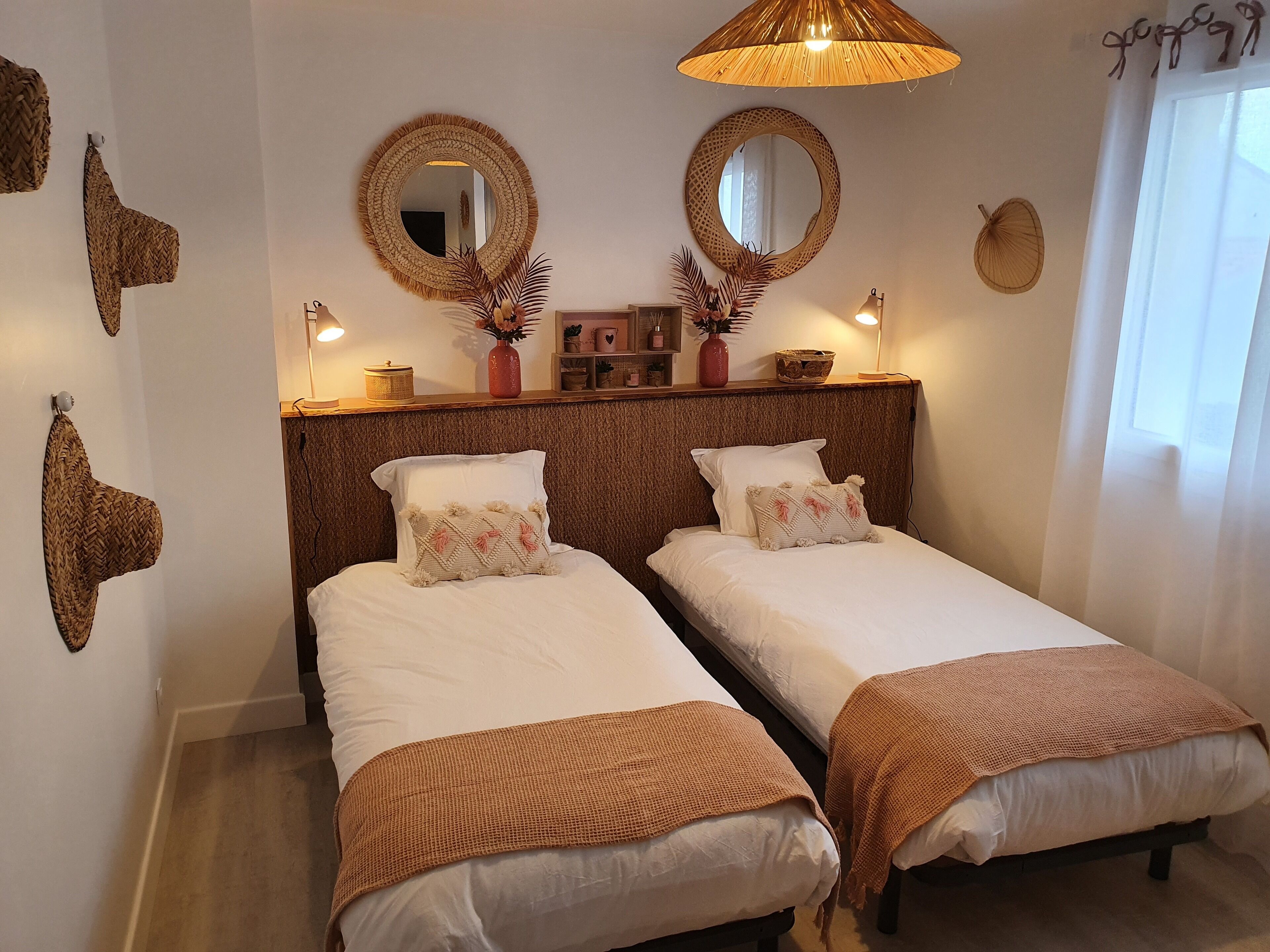 Ein Zimmer mit zwei Einzelbetten, einem Holzkopfende, gewobenen Wanddekorationen und einer hängenden Leuchte.
