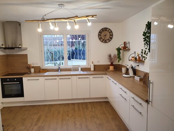 A modern kitchen with white cabinets, a wooden countertop, a built-in oven, and a large window with a view of trees.