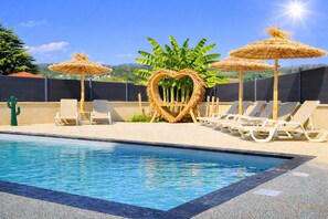 A swimming pool with lounge chairs and thatched umbrellas, surrounded by greenery.