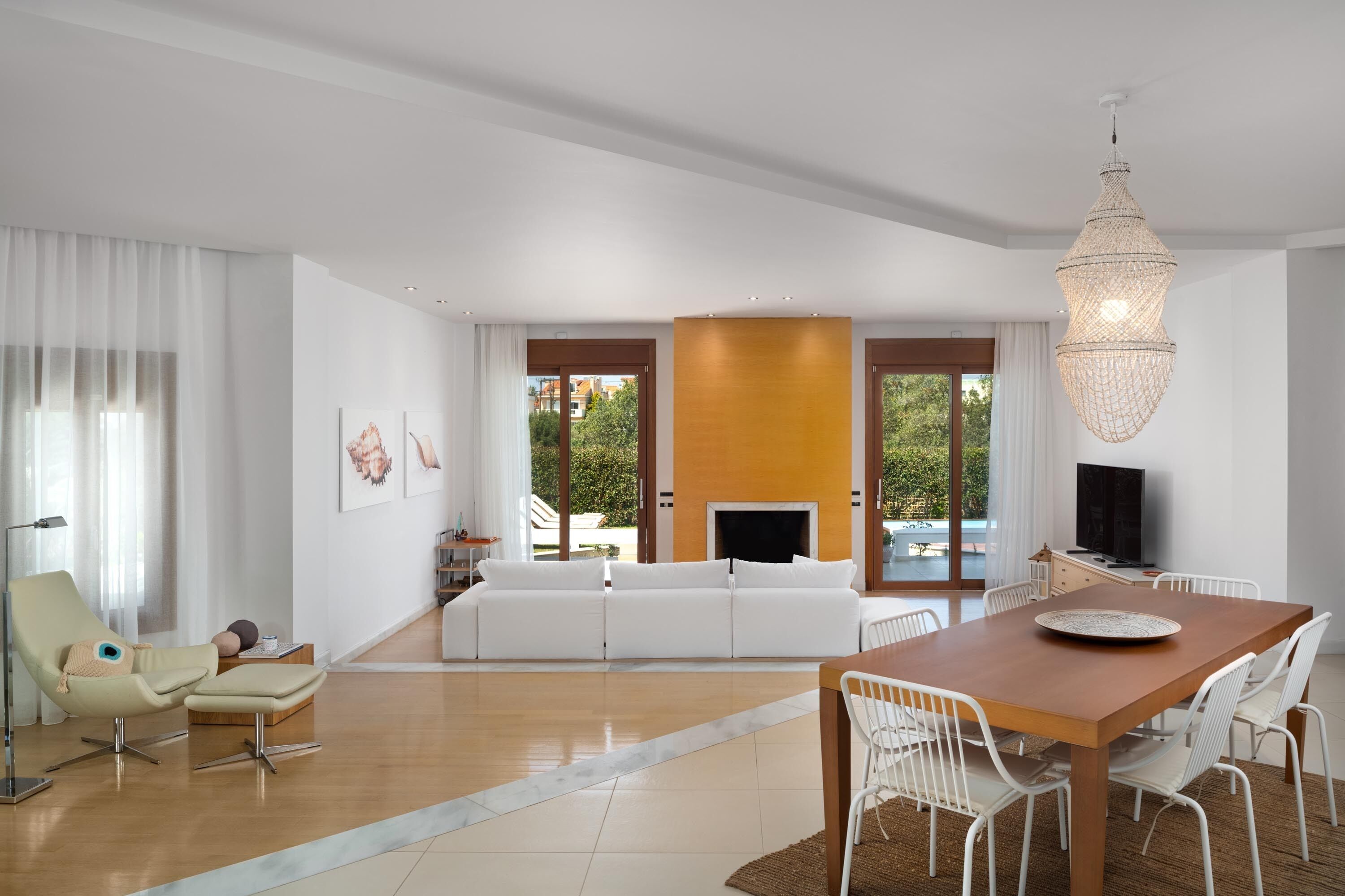 Een moderne woonkamer met een bank, een eettafel, stoelen, een televisietoestel en een kroonluchter.