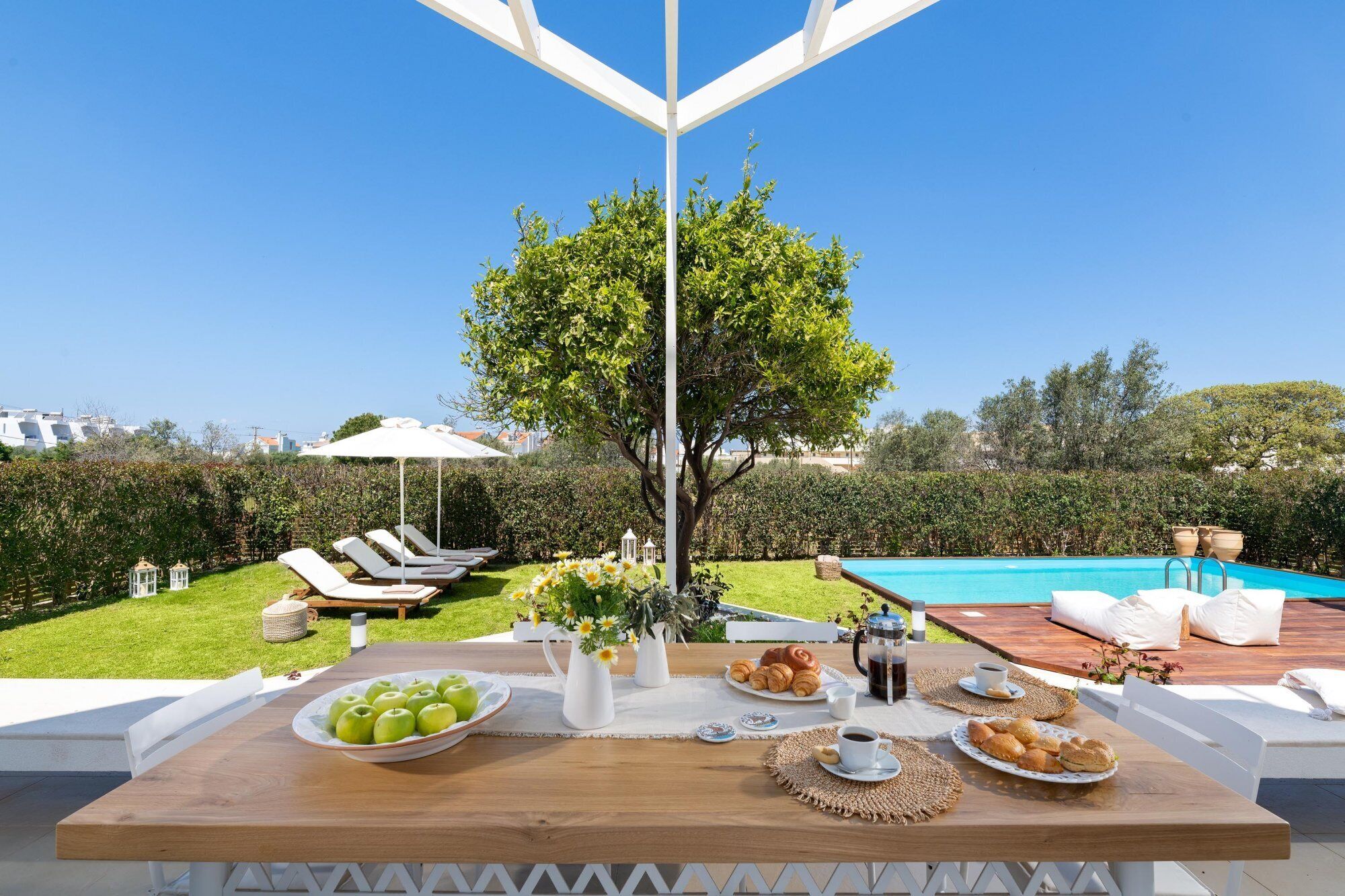 Area pranzo a bordo piscina con tavolo apparecchiato per la colazione, poltrone relax e vista sulla piscina.