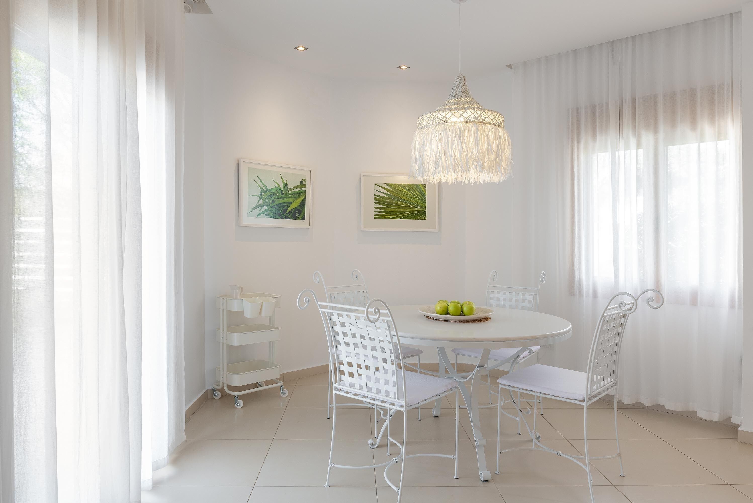A dining area with a round table, white chairs, a chandelier, and artwork on the walls.
