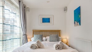 A neatly made bed with pillows and rolled towels, a framed picture above it, and a radiator on the wall. - Constantine Bay Cottage (Padstow)