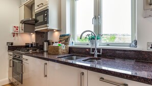 A modern kitchen with stainless steel appliances, a granite countertop, and a window with a view of greenery. - Constantine Bay Cottage (Padstow)