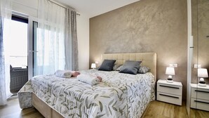 Um quarto com cama, mesas de cabeceira, um espelho e vista para o exterior.