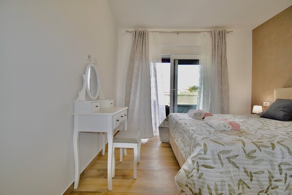 A bedroom with a bed, a bedside table with a mirror, a chair, and a window with curtains.