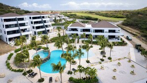 A resort with a central pool, multiple buildings, and a view of the surrounding landscape. - Blue Bay | The Reef | Terrace (Sint Michiel)