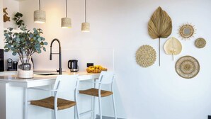 A modern kitchen with white bar stools, a coffee machine, and decorative wall art. - Blue Bay | The Reef | Terrace (Sint Michiel)