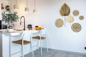 Una cocina moderna con taburetes blancos, una cafetera y decoración en la pared.