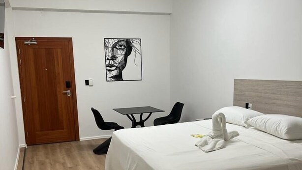 Ein Hotelzimmer mit Bett, Schreibtisch und Stuhl. Eine Tür und eine Wandleuchte sind ebenfalls vorhanden.