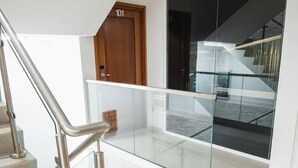 Ein modernes Interieur mit einer Treppe, einer Holztür mit der Bezeichnung '101' und einem gläsernen Geländer, das auf einen Balkon blickt.