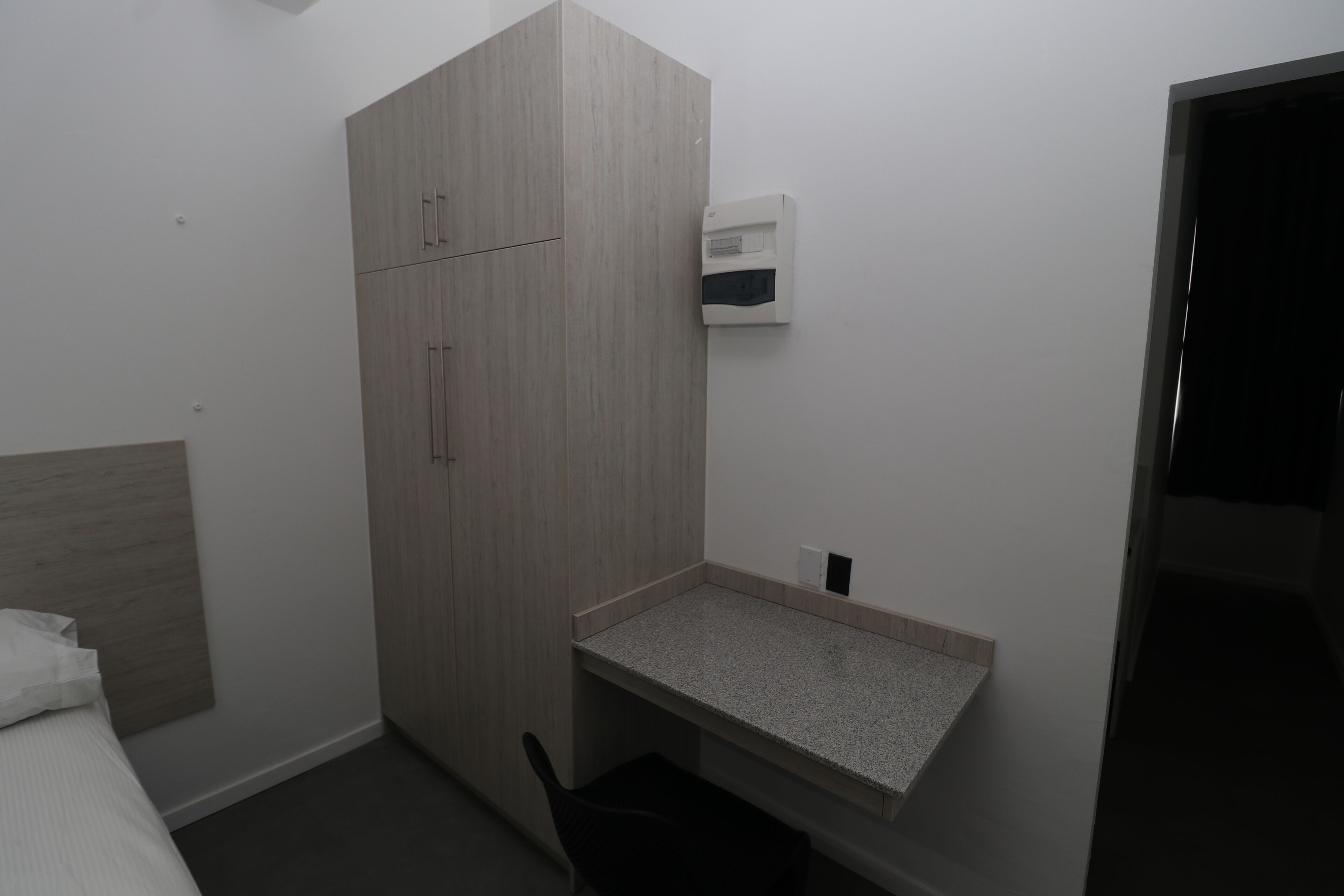 Una habitación pequeña y moderna con una cama, un armario de madera, un escritorio pequeño y un equipo de aire acondicionado instalado en la pared.