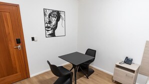 Ein Zimmer mit Holztür, einem schwarzen Tisch mit vier Stühlen, einem an der Wand befestigten Kunstwerk und einem kleinen Nachttisch mit einem Telefon.