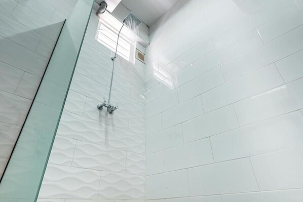 Un baño con azulejos blancos, mampara de vidrio y ducha visible.