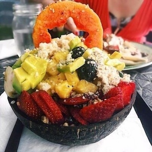 A bowl of fruit salad with strawberries, mango, and other fruits, topped with a sesame seed bun. - Outstanding Oceanfront Studio - Kona Islander Inn Condos Condo by RedAwning (Kailua-Kona)