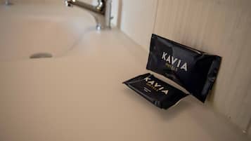 Un lavamanos de baño con dispensador de toallas y un paquete negro con la etiqueta "KAVIA HOTELS" en la pared.