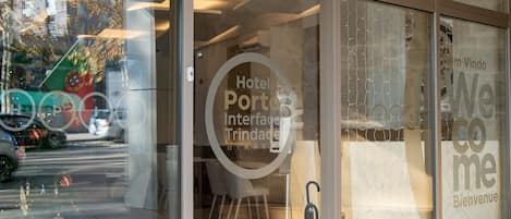 Entrada de un hotel con puerta de cristal, número de habitación visible y cartel de bienvenida.