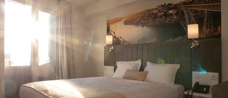 Quarto de hotel com uma cama grande, mesa de cabeceira com abajur e um mural na parede de uma ponte.