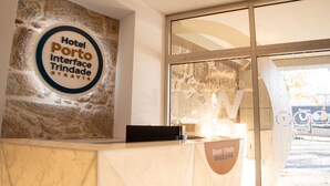 A hotel reception desk with a stone wall backdrop and a sign that reads "Hotel Porto Interface Trindade SYKAVIA." - Hotel Porto Interface Trindade By Kavia (Porto)