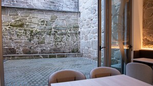 A stone-walled room with a tiled floor, a table, and two chairs. - Hotel Porto Interface Trindade By Kavia (Porto)
