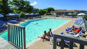 A swimming pool with lounge chairs and umbrellas, surrounded by greenery and buildings. - At the end of the garden, the pine forest and the beach (Poggio-Mezzana)