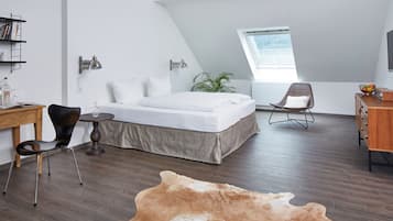 A modern bedroom with a sloped ceiling, a bed, a desk, a chair, a small table, a potted plant, and a large rug.